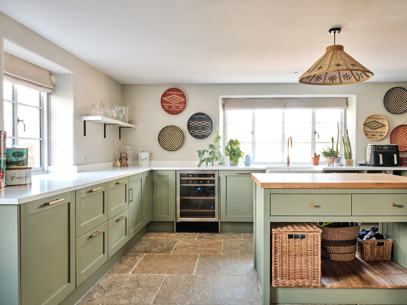 Sage-green kitchen cabinetry, stone floor and timber worktops